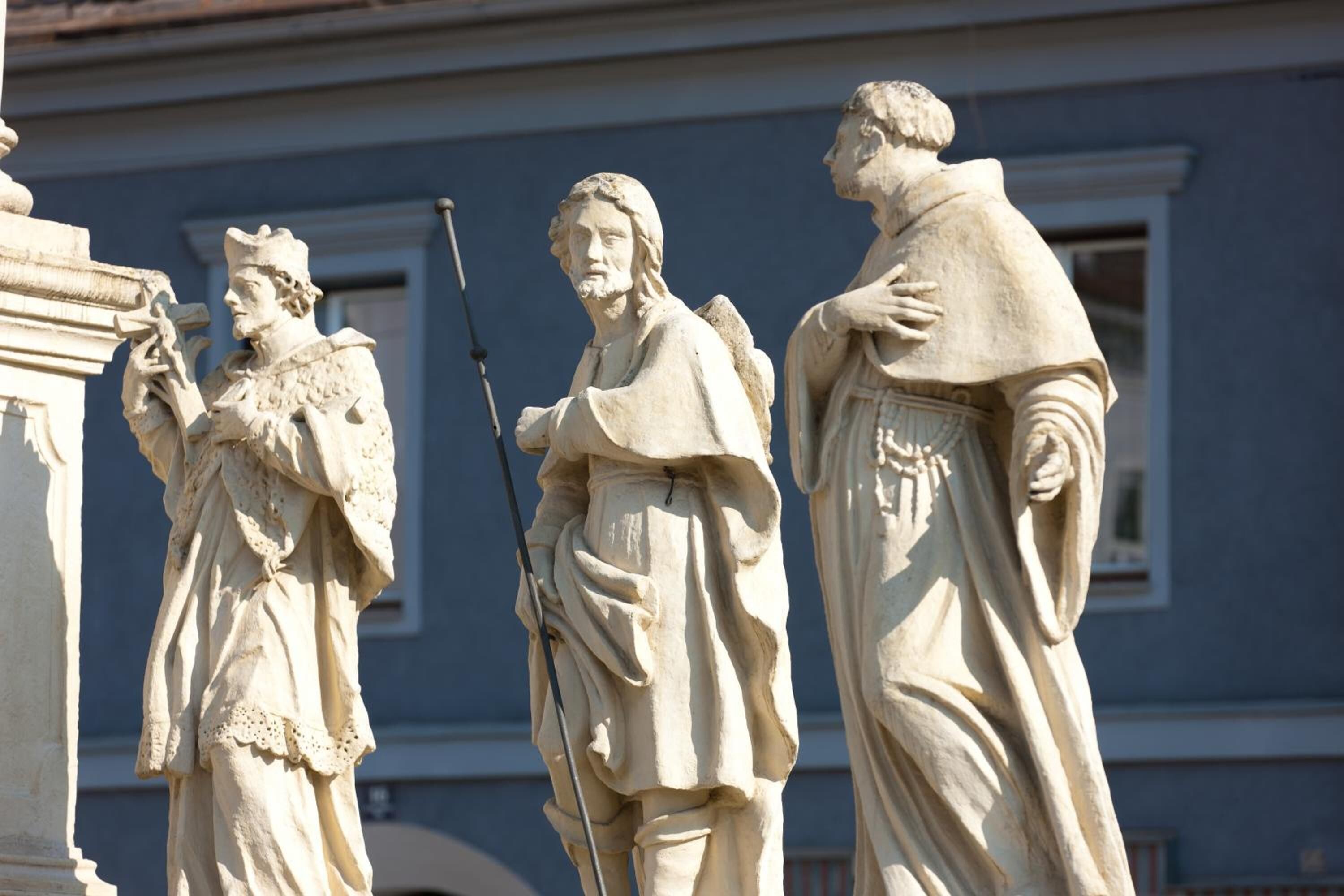 Una estatua de tres figuras con vestimenta clásica, ubicada frente a una fachada de edificio.
