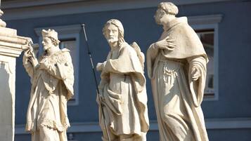 Una estatua de tres figuras con vestimenta clásica, ubicada frente a una fachada de edificio.