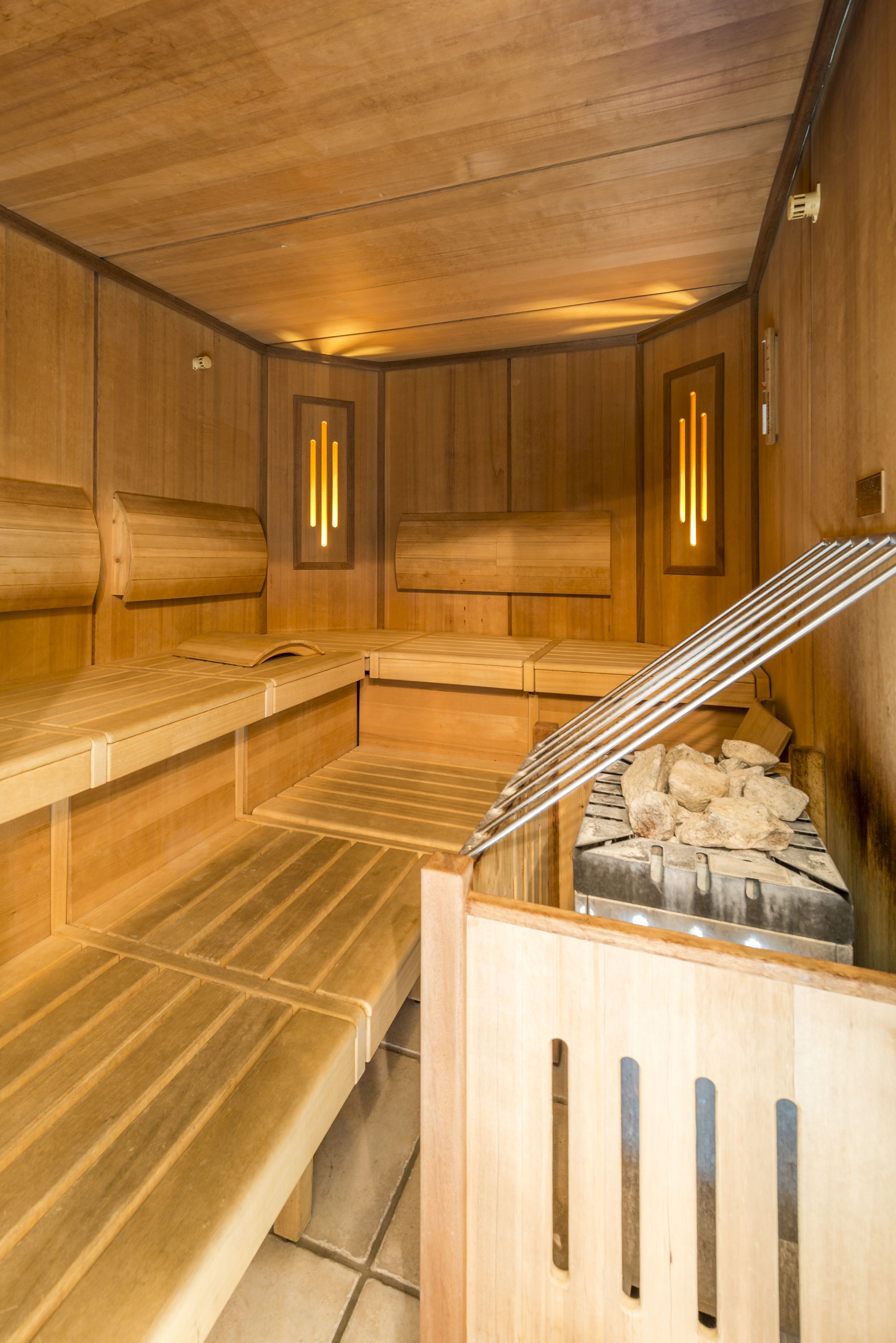 A sauna with wooden benches and a stone bench, wooden walls, and a ceiling with a light fixture.