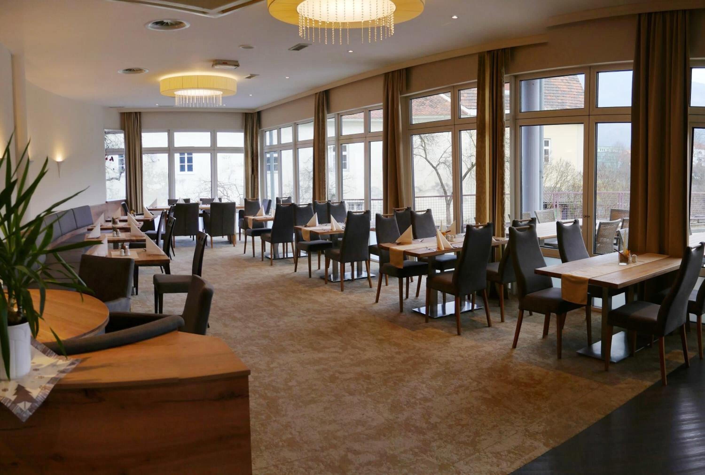 Un vaste espace dédié à la salle à manger, avec de nombreuses tables et chaises, de grandes fenêtres et un lustre.