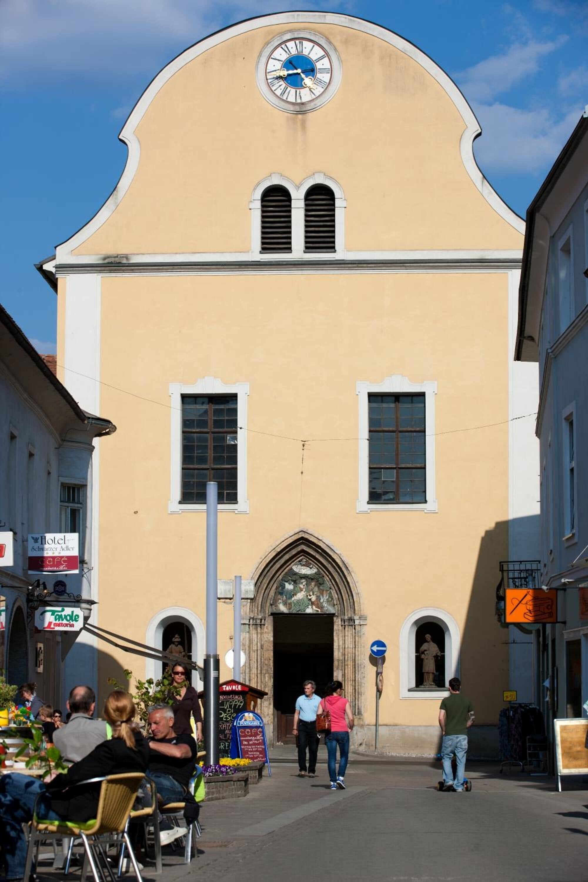 A building with a clock, a large arched entrance, and a sign for a cafe.