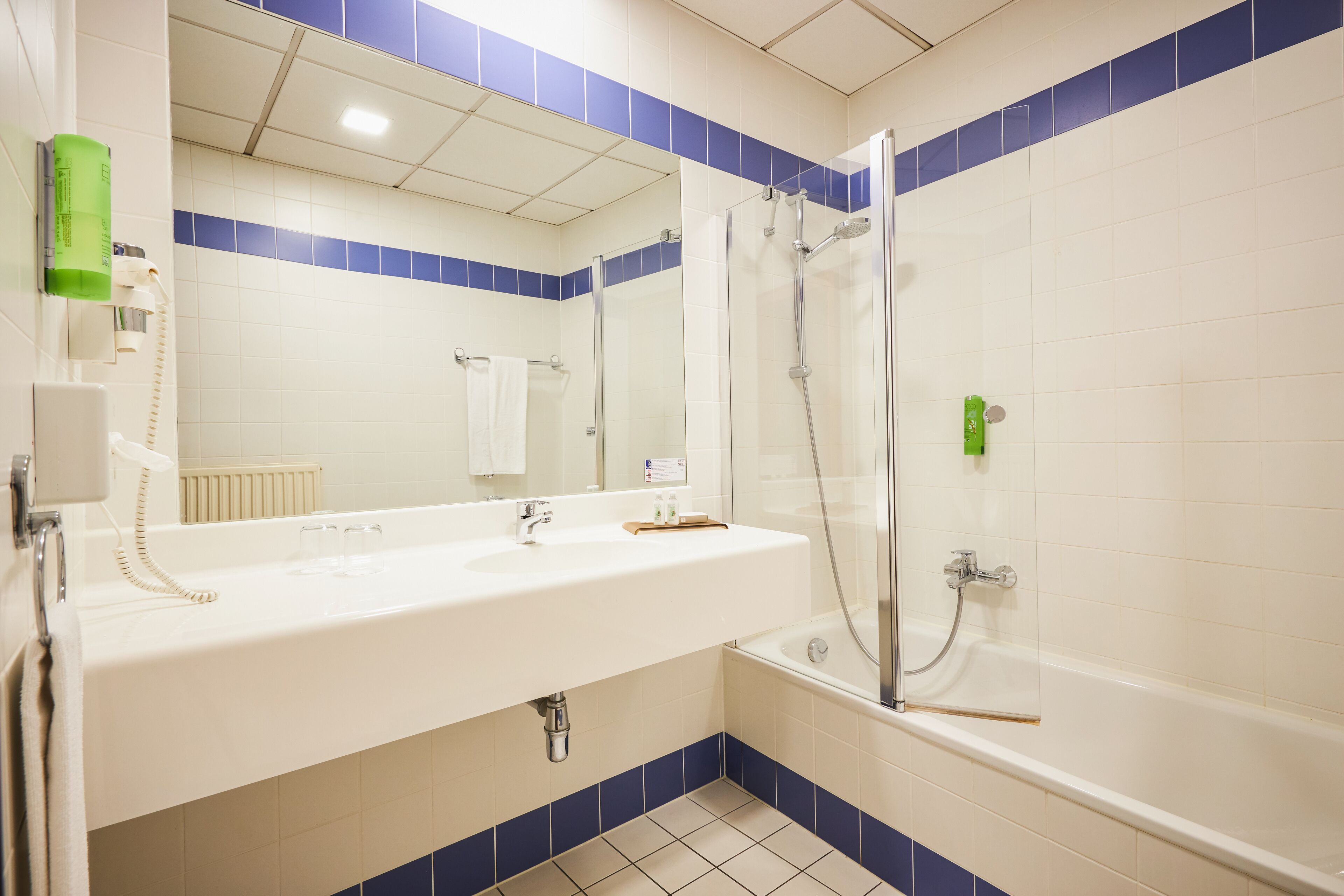 A bathroom with a white sink, a mirror, a glass-enclosed shower, and blue-tiled walls.