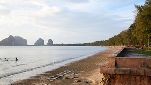 A beach with a concrete barrier, calm water, and distant rocky formations. - PK Resort (Sikao)
