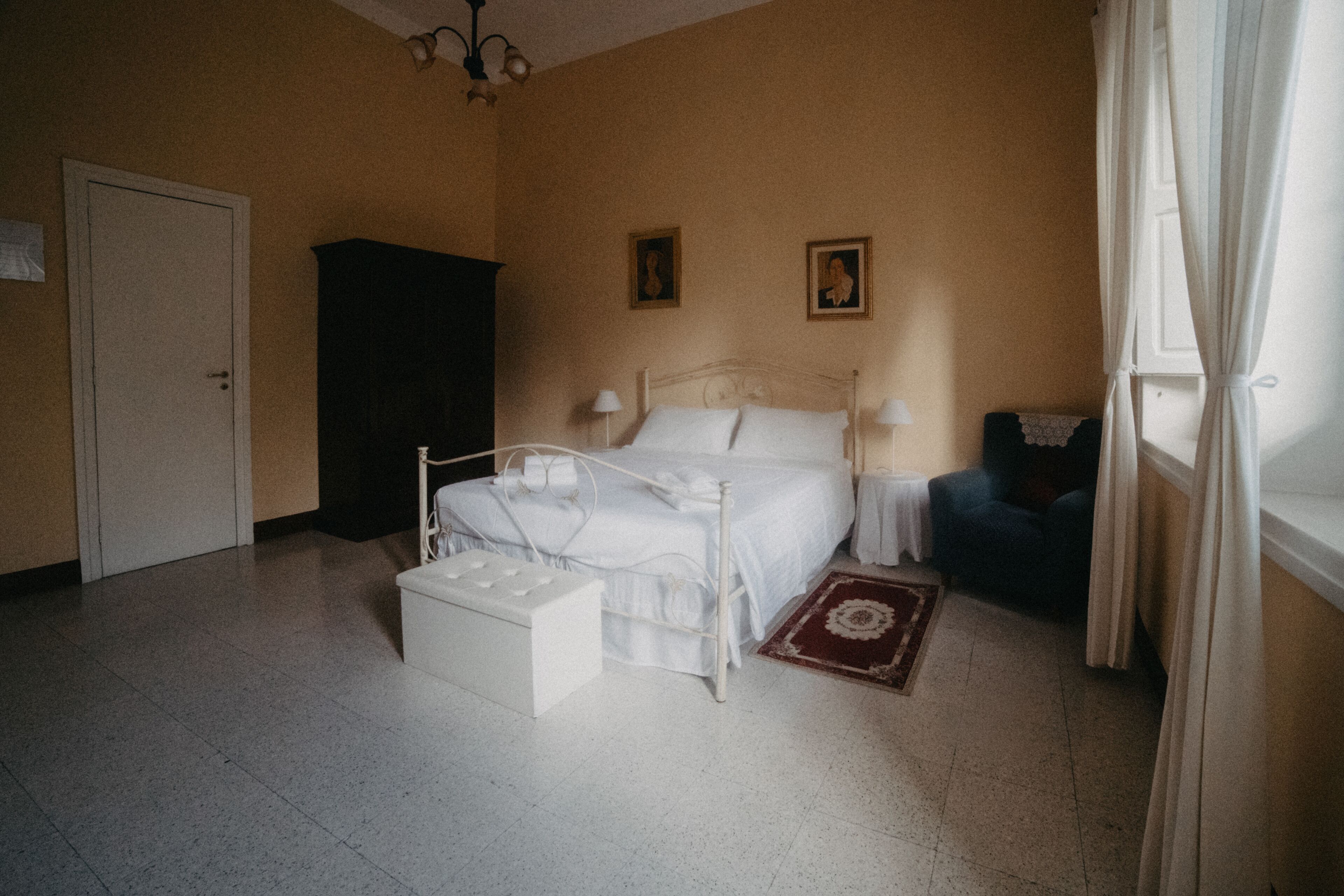 A bedroom with a bed, bedside tables, a wardrobe, a chair, and a window with curtains.