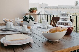 Una mesa de madera dispuesta con platos, tazones, vasos y una jarrón, con vistas a un balcón al fondo.