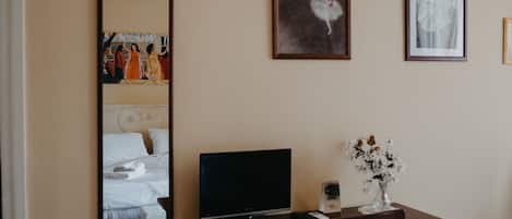 A hotel room with a bed, a TV, a desk with a vase of flowers, and framed artwork on the wall.