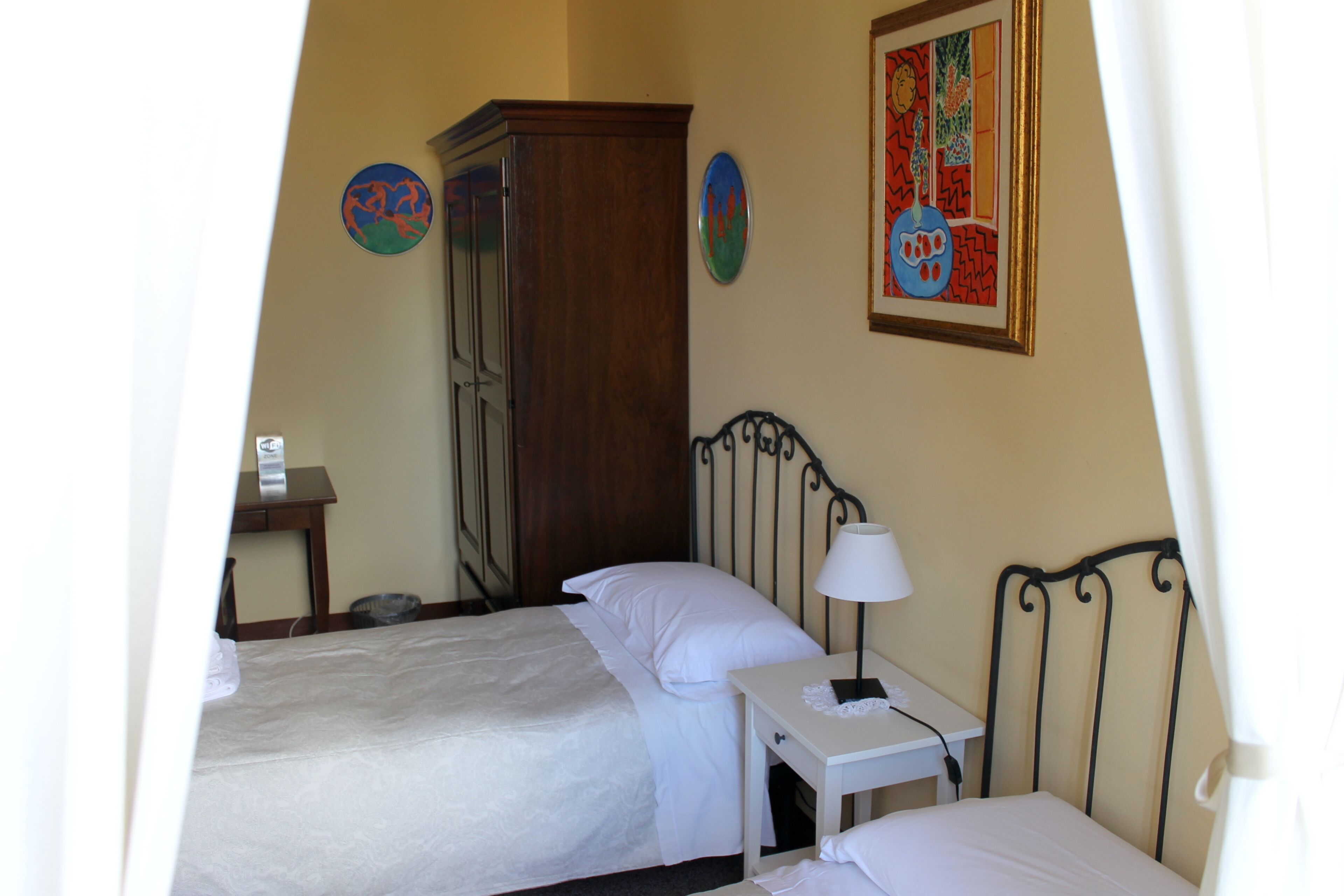 A bedroom with a bed, a bedside table with a lamp, a wardrobe, and two wall decorations.