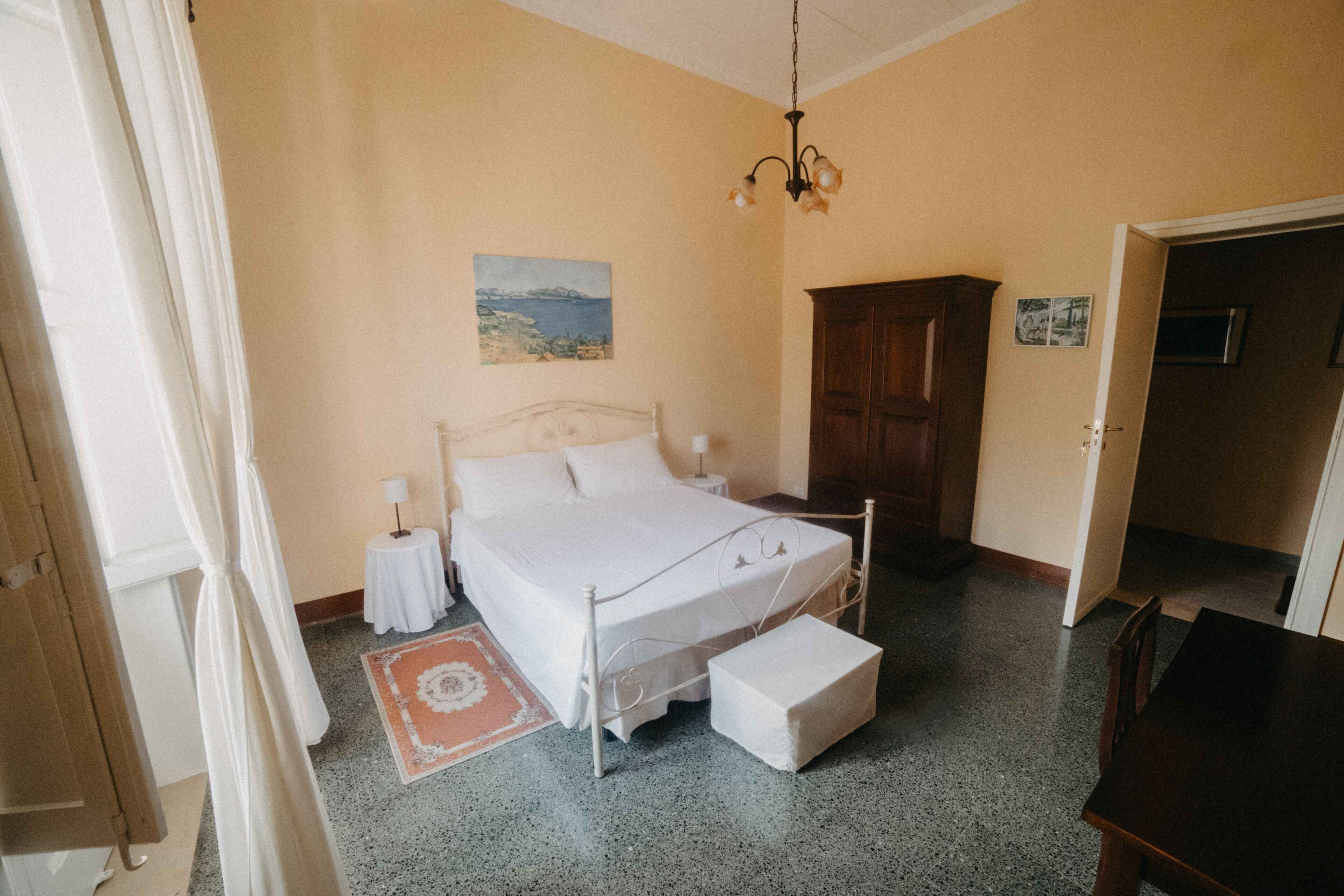 A bedroom with a bed, bedside tables, a nightstand, a wooden wardrobe, and a door leading to another room.