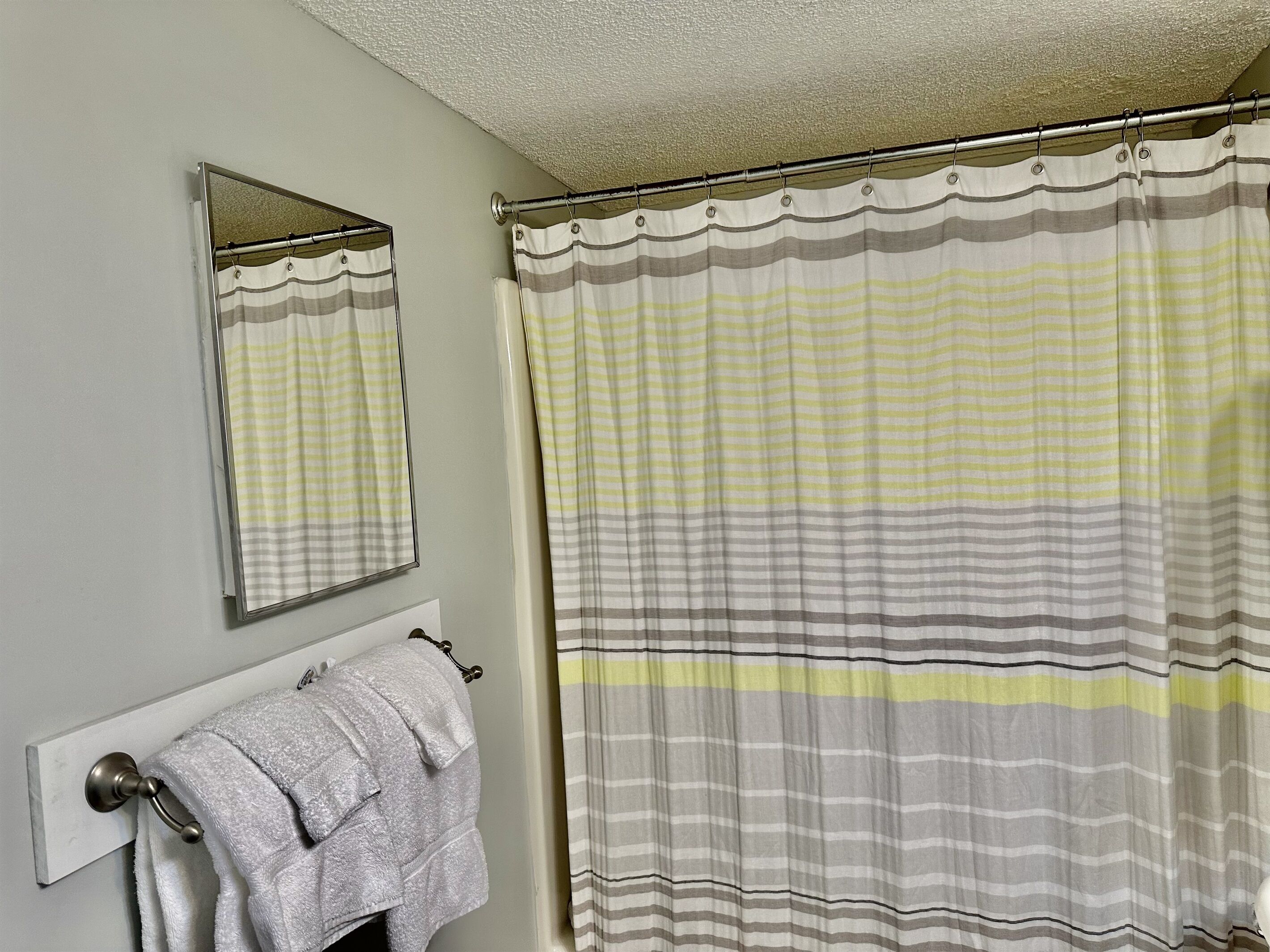 Une salle de bain avec un porte-serviettes sur lequel est pliée une serviette, un miroir et un rideau de douche à rayures.