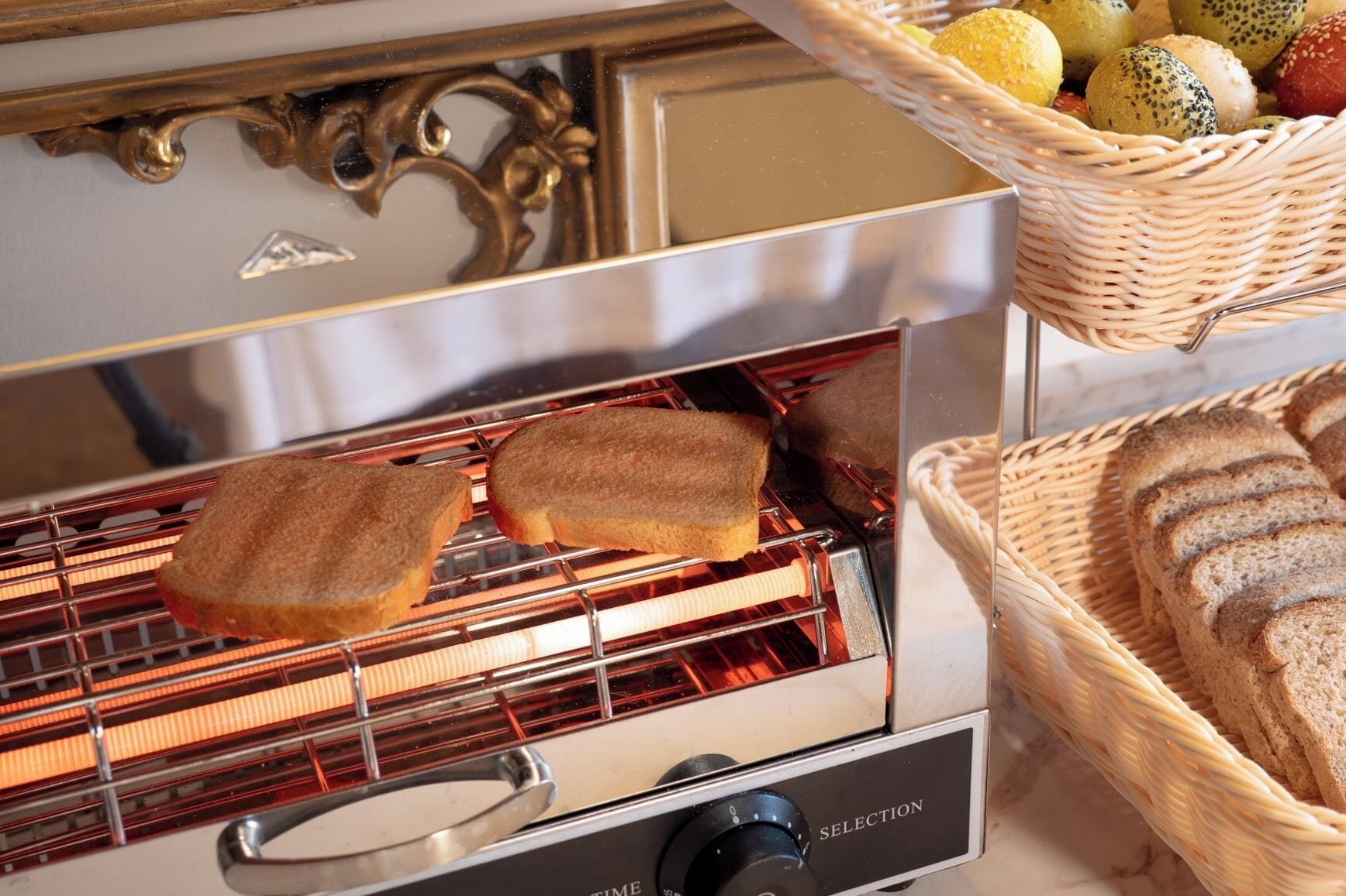 Un horno tostador con dos rebanadas de pan tostándose, una cesta de panecillos y una cesta de productos horneados variados.