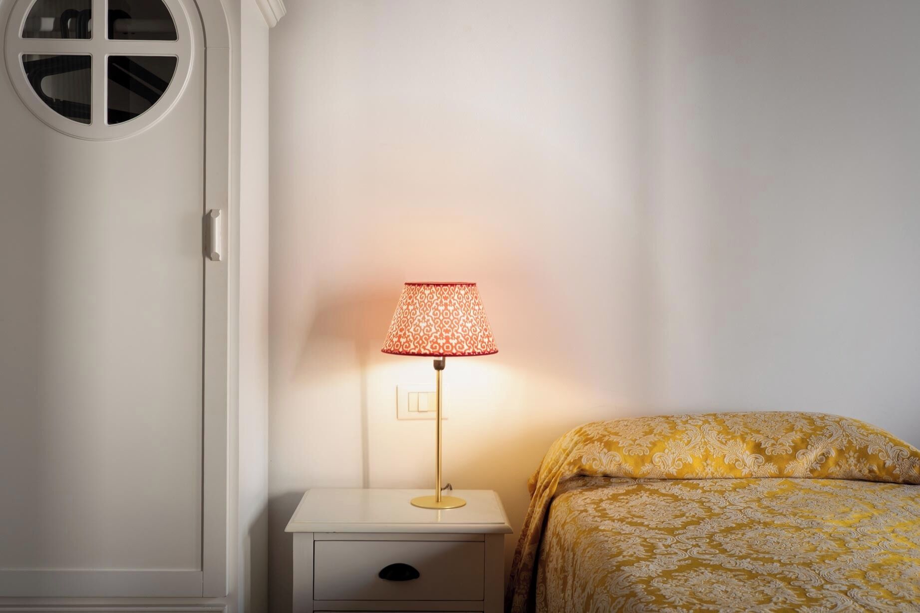 A bedroom with a bedside table, a lamp, and a bed with patterned bedding.