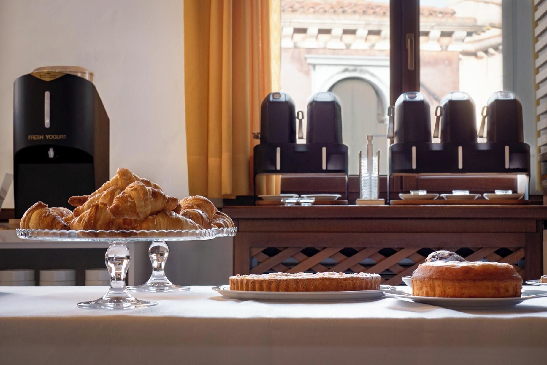 A breakfast buffet with croissants, a cake, and a coffee machine.
