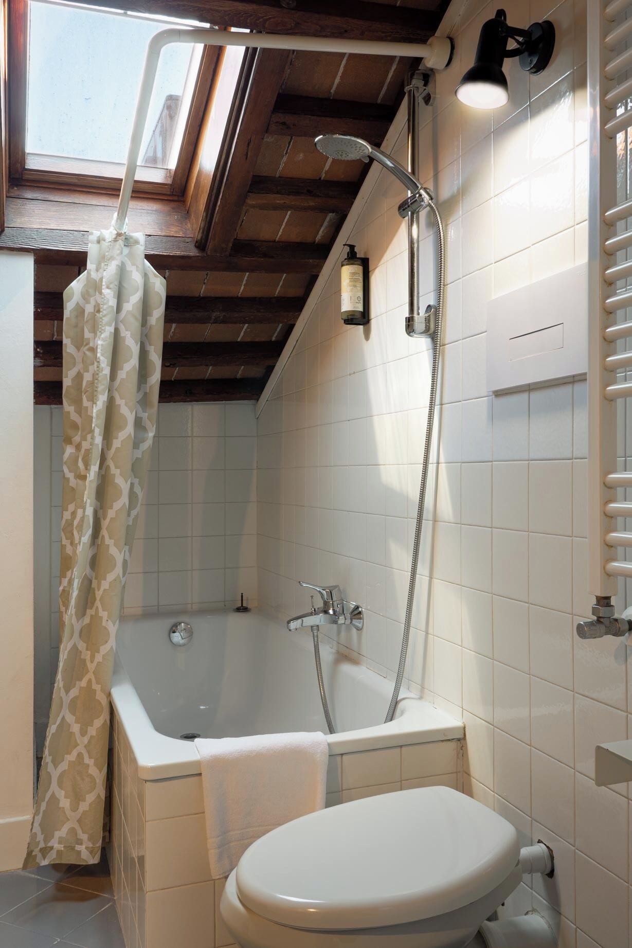 Une salle de bain avec une baignoire, des toilettes, un rideau de douche et une lucarne.