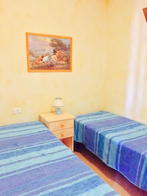 A room with two beds, a nightstand with a lamp, and a painting on the wall. - Palau Apartment (Palau)