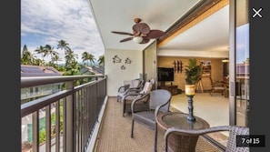 Relax on the balcony with a view of palm trees and a clear sky, surrounded by wicker chairs and a flat-screen TV.
