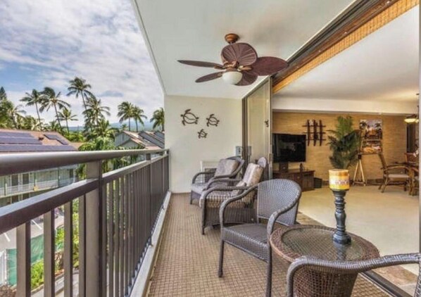 A balcony with wicker furniture, a ceiling fan, and a view of palm trees. - KJ’s Place, in the heart of the city. (Kailua-Kona)