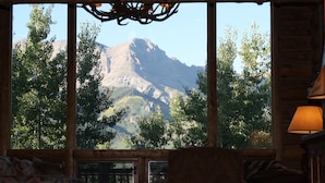 L’intérieur d’un chalet chaleureux, avec une grande fenêtre donnant sur une vue imprenable sur une montagne.