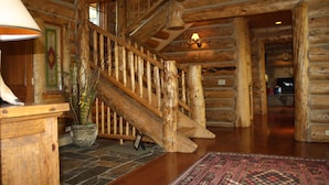 Un escalier en bois au design rustique, un sol en pierre et un tapis à motifs.