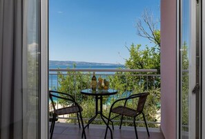 A balcony with a table and chairs, overlooking a body of water and greenery. - Tourist Settlement Brzet (Omis)