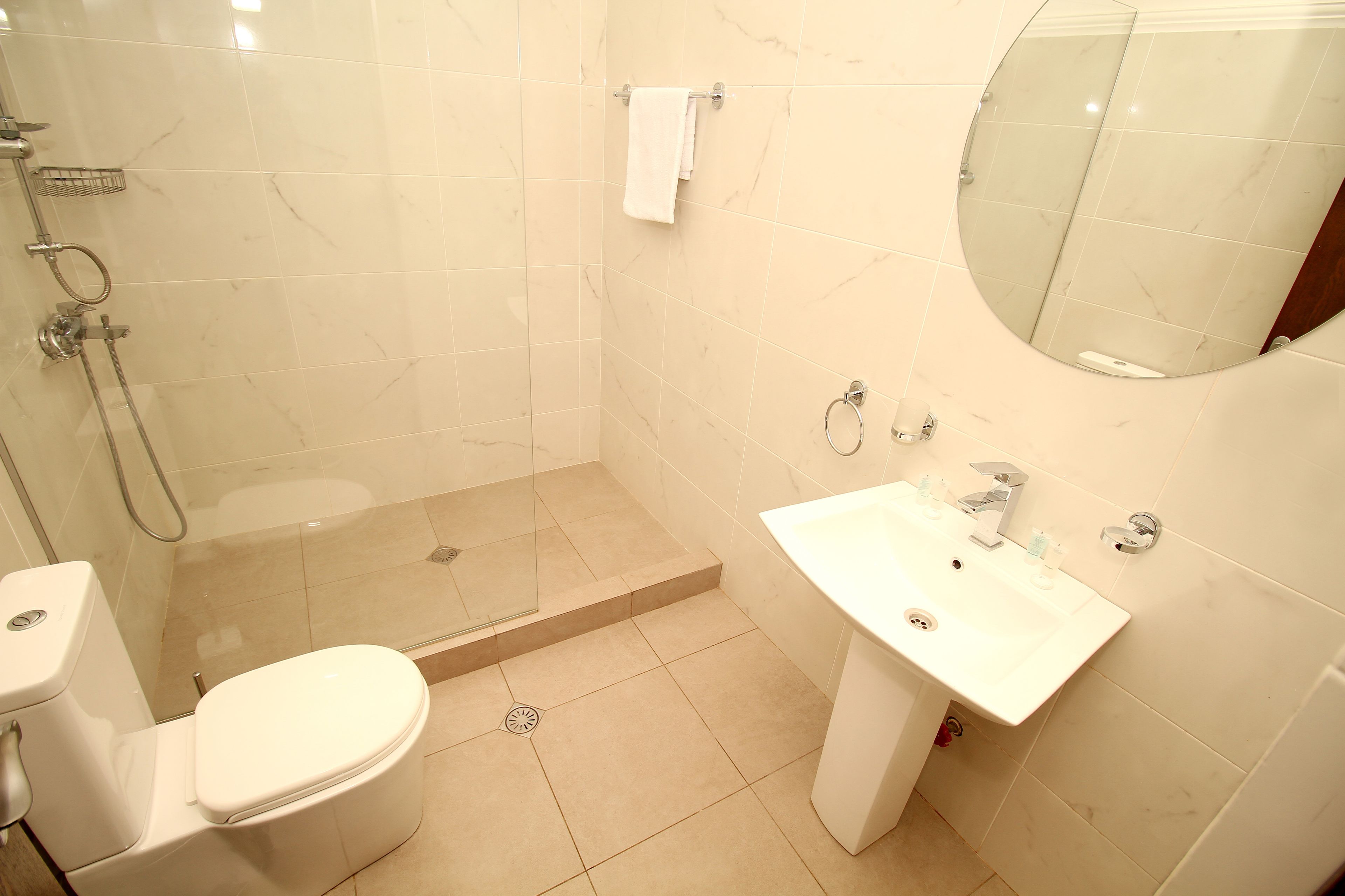 A bathroom with a toilet, shower, sink, and mirror.