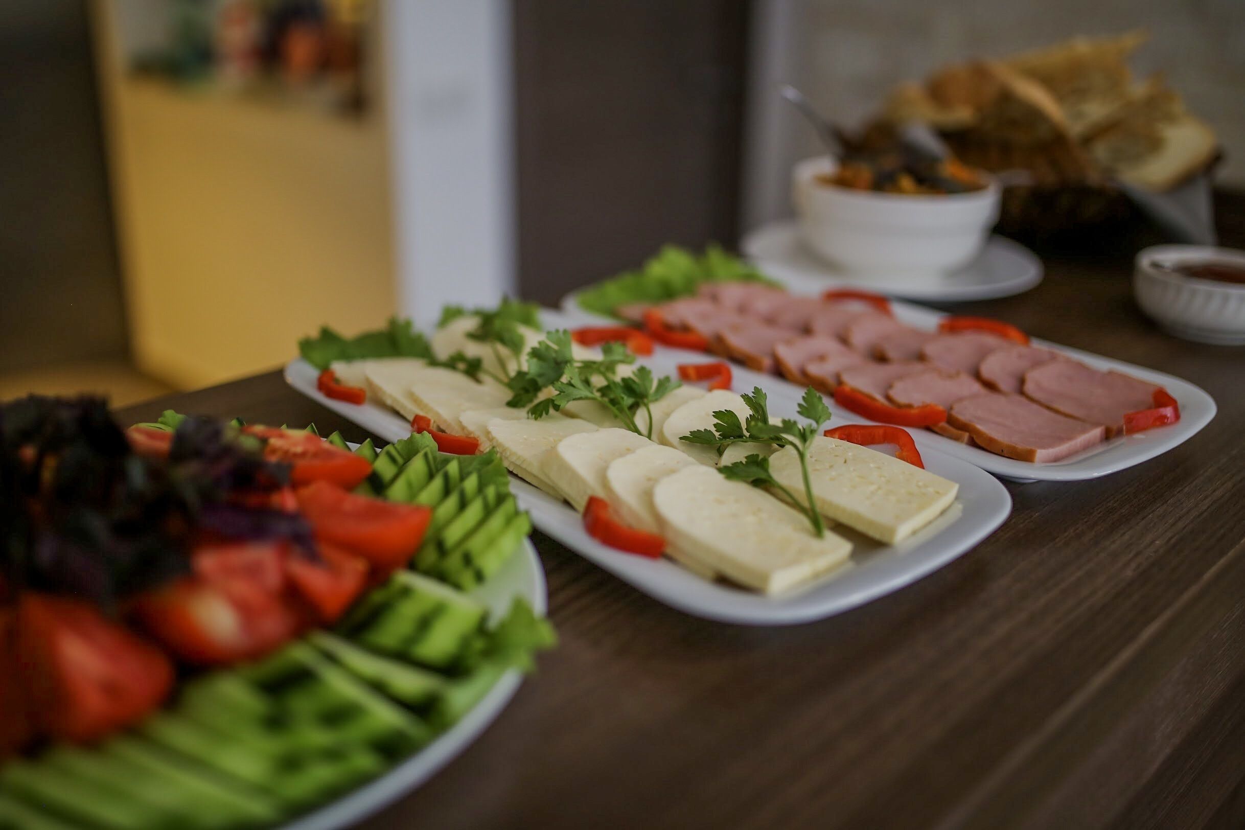 Una mesa con diversos alimentos, como jamón en rodajas, queso y verduras.