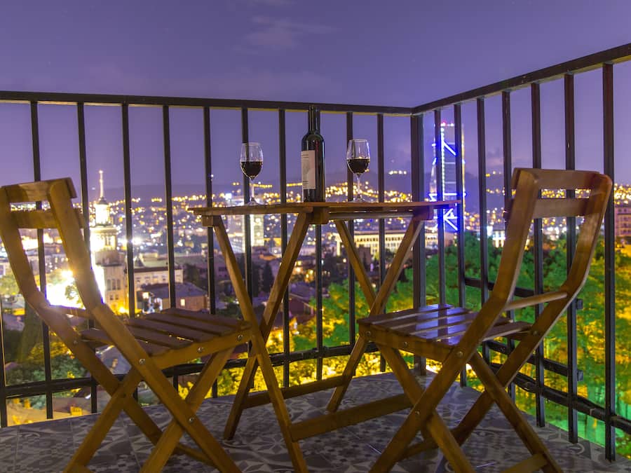 A balcony with two wooden chairs and a table, a bottle of wine, and two wine glasses.