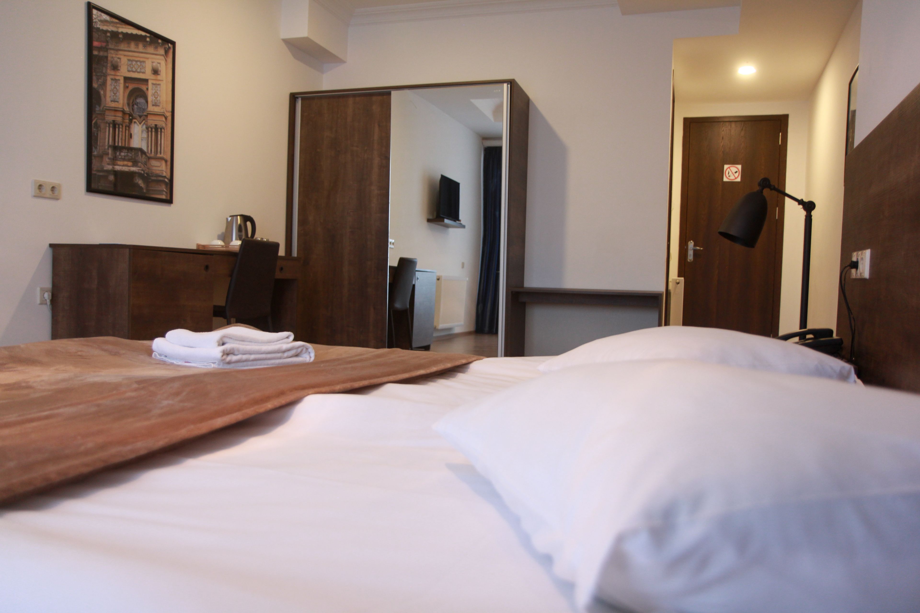 Een hotelkamer met een bed, een houten hoofdbord, een bureau met stoel, een flatscreen televisie en een deur met een 'verboden toegang'-bord.