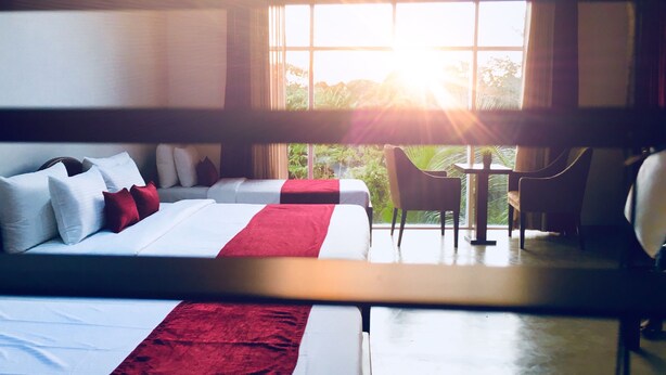 A hotel room with a large bed, a smaller bed, a desk, and a chair. There is a window with a view of greenery outside. - 8 Plus  Villa (Battaramulla)