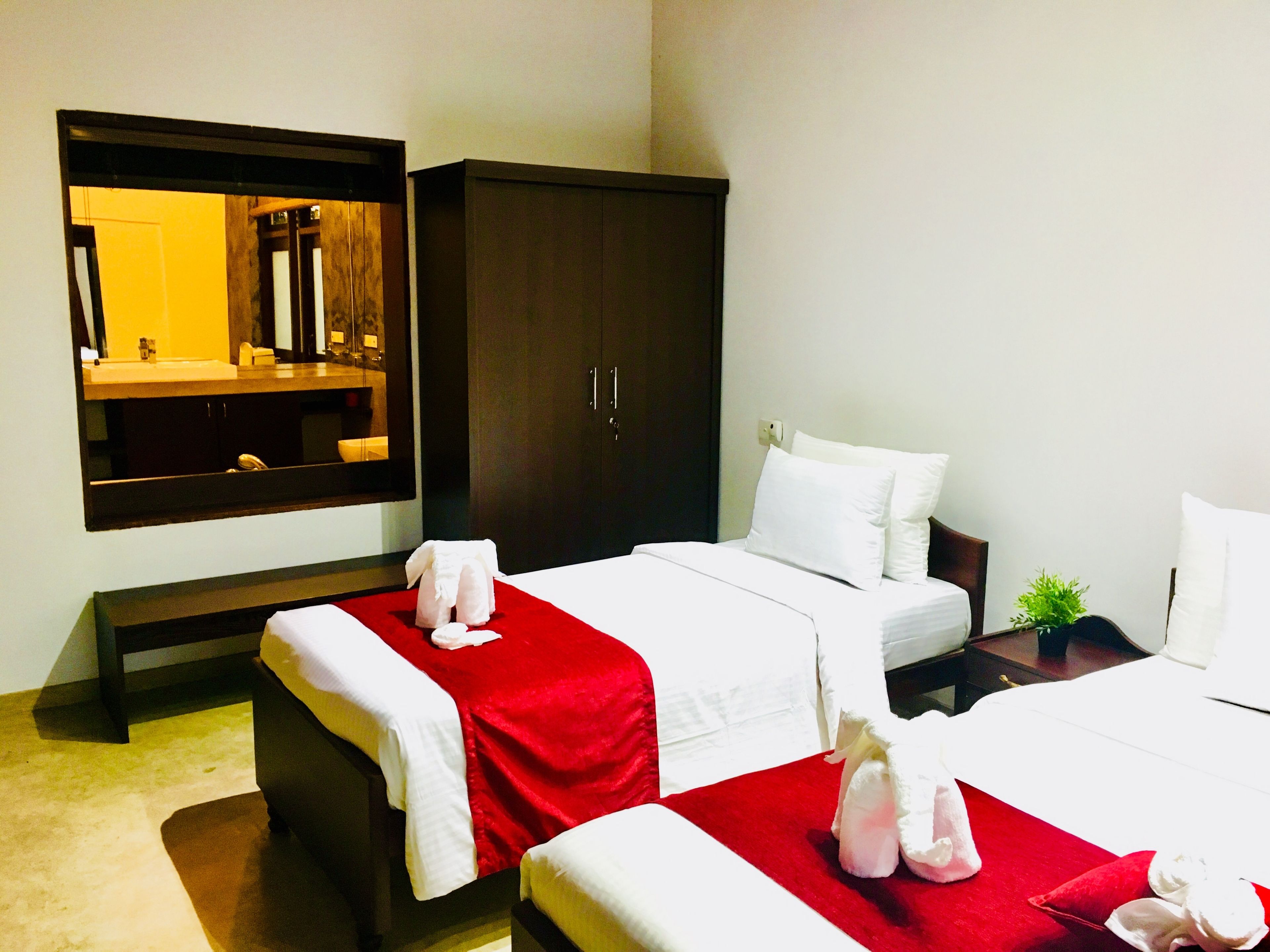 A hotel room with two beds, a large mirror, a wardrobe, and a small plant.