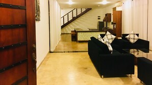 A modern living room with a black sofa and a coffee table, a staircase leading to a kitchen, and a wooden door. - 8 Plus  Villa (Battaramulla)