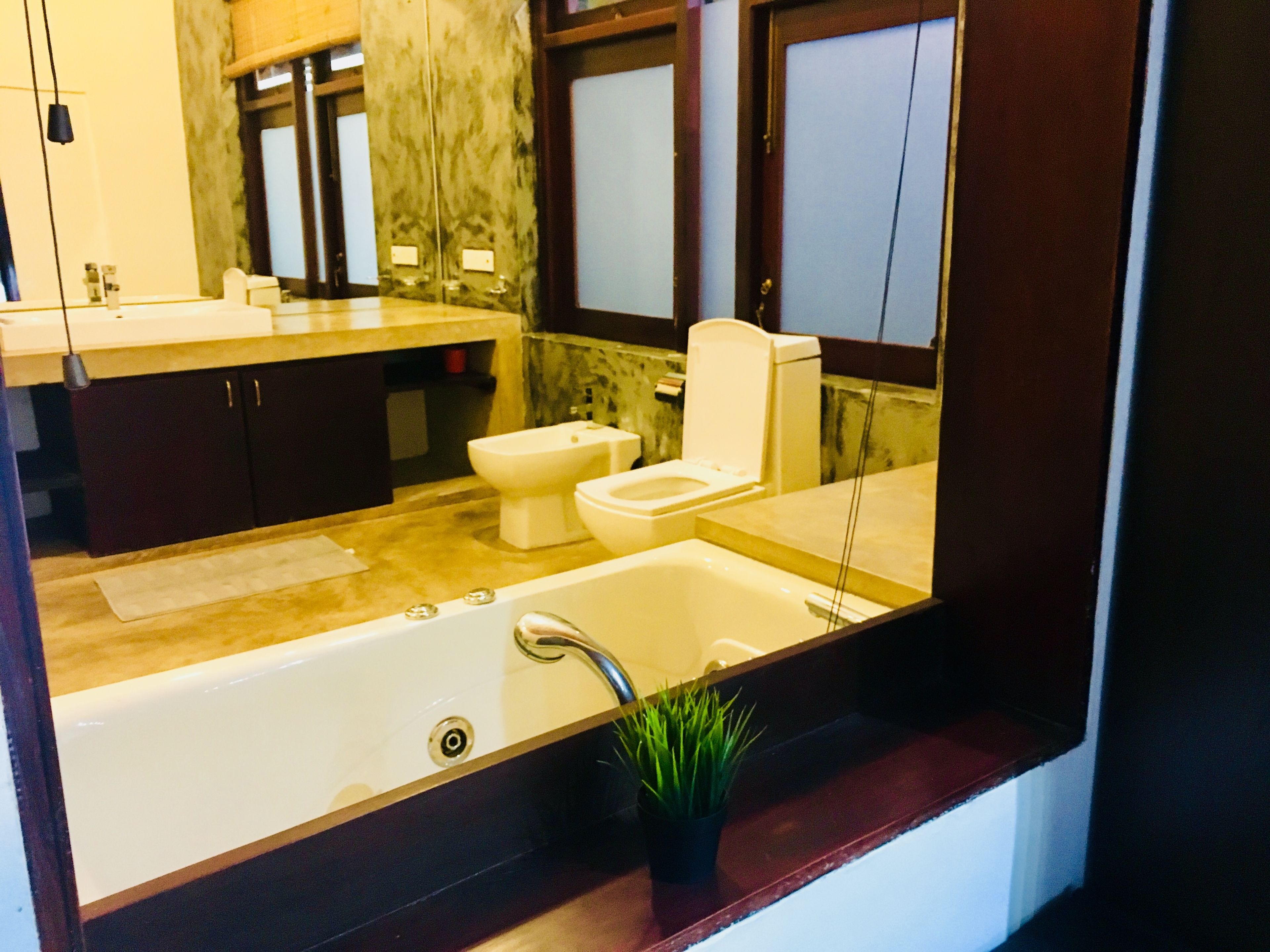 A modern bathroom with a bathtub, toilet, and bidet. It features marble countertops, dark cabinetry, and a large mirror.