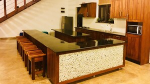 A modern kitchen with a central island, wooden cabinets, and a built-in stove. - 8 Plus  Villa (Battaramulla)