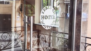Entrada com porta de vidro, guarda-corpo de metal e uma placa com a inscrição 'Hotel'.