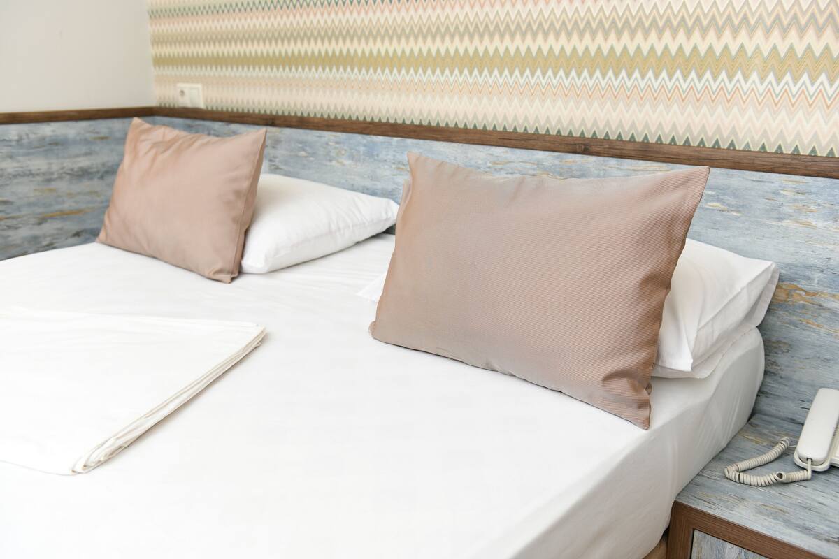 Une chambre d’hôtel avec un lit, deux oreillers, une table de chevet avec un téléphone et un mur décoré d’un motif.
