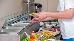 Disposição de buffet com diversos alimentos e uma chaleira a vapor ao fundo.