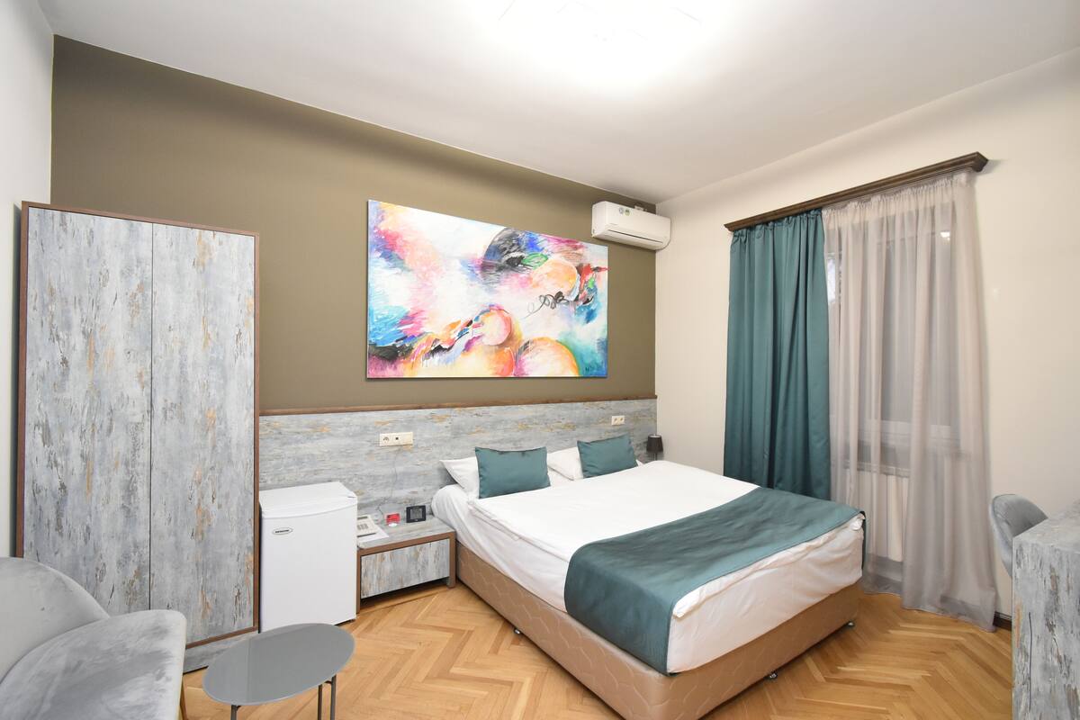 Une chambre d’hôtel moderne avec un grand lit, un bureau, une chaise et un tableau au mur.