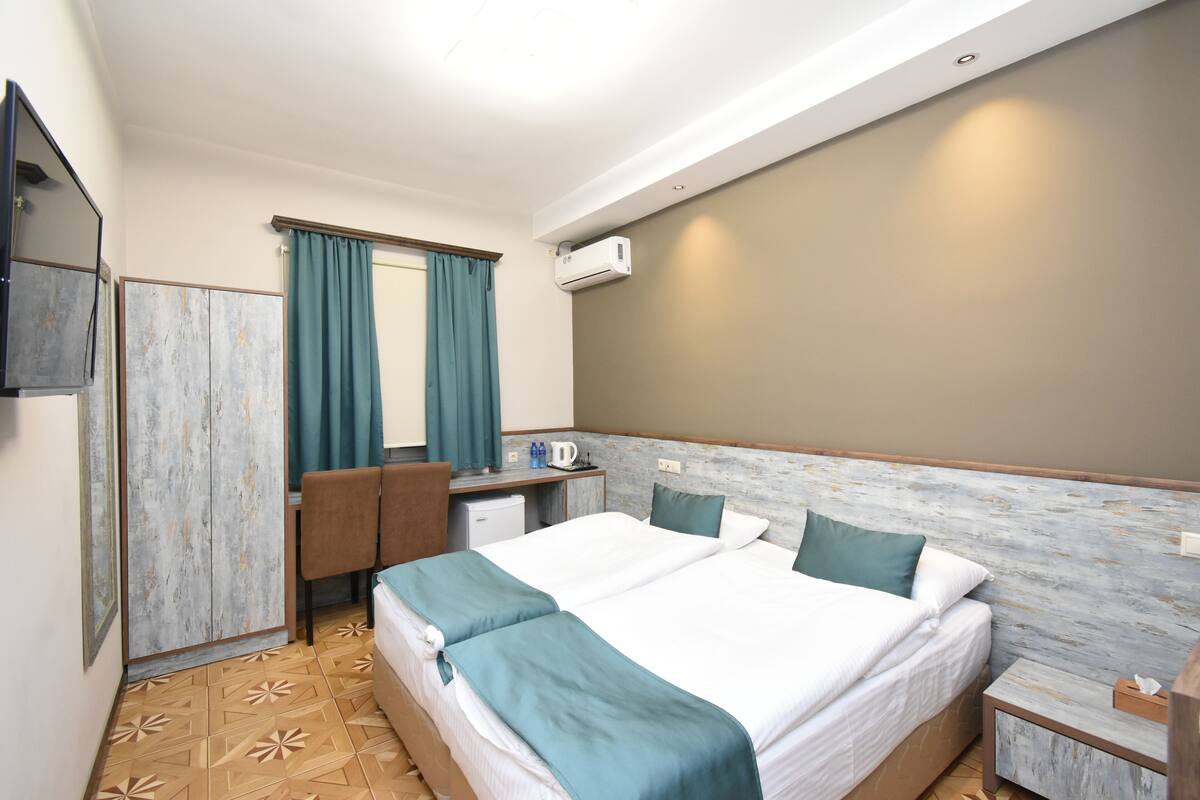 Une chambre d’hôtel avec un lit double, un bureau avec une chaise, une petite kitchenette et un téléviseur fixé au mur.