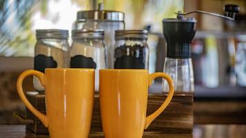 Deux tasses jaunes sur une surface en bois, avec des bocaux et un moulin à café en arrière-plan.