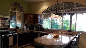 Una cocina con una isla grande, estufa y ventana con vista a la vegetación.