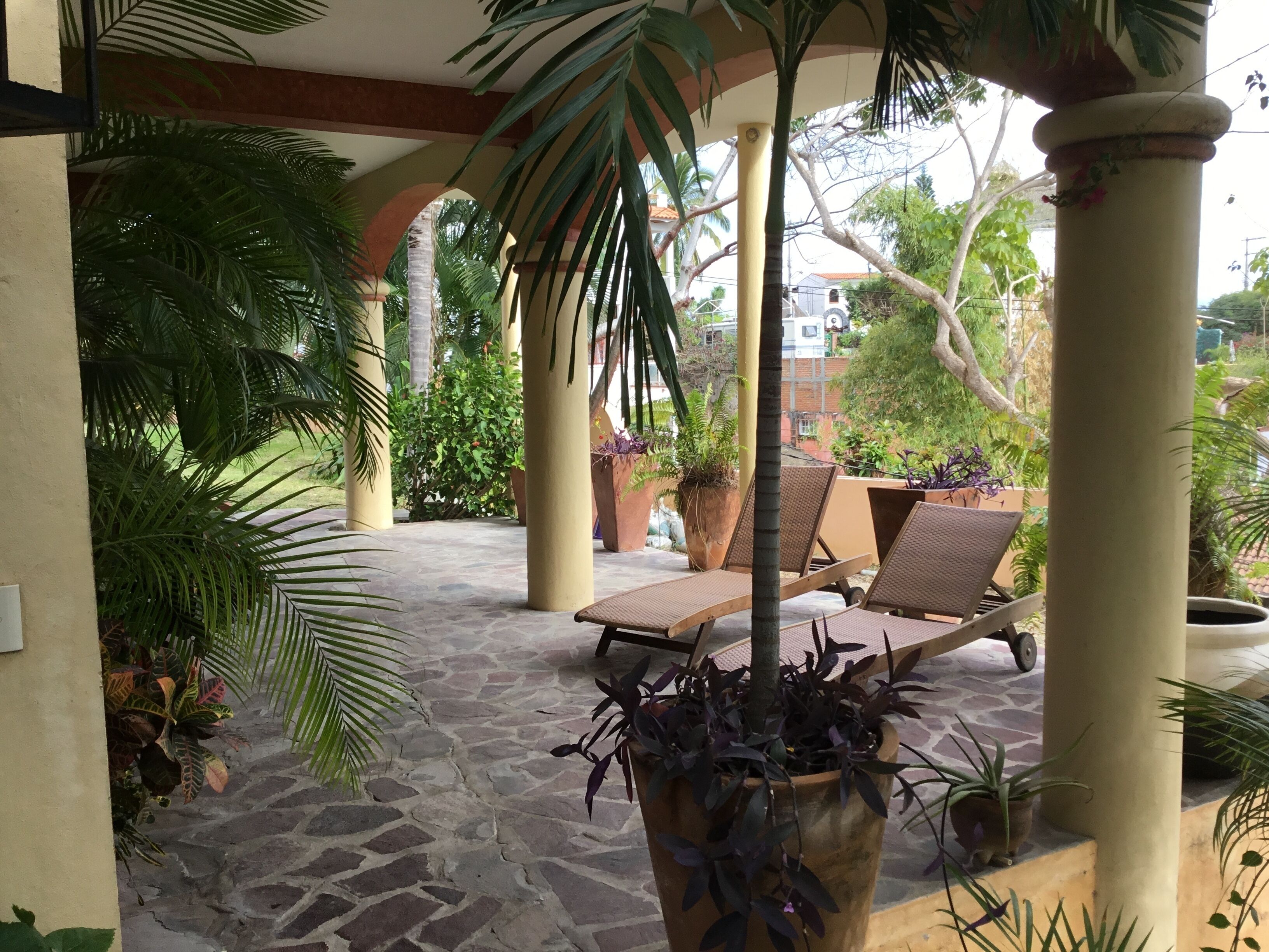Un espace extérieur abrité, doté d’un sol en pierre, de chaises longues et de plantes en pot.