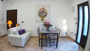 A living room with a white sofa, a dining table with chairs, a vase of flowers, and a lamp. - Two apartments for groups or families up to 9 In St. Peter area, courtyard (Roma)