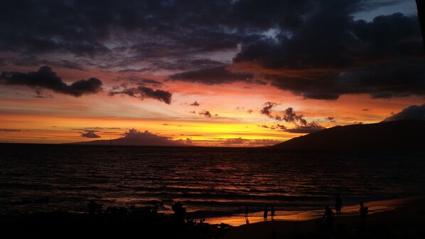 A sunset over a body of water with silhouettes of people on the shore.