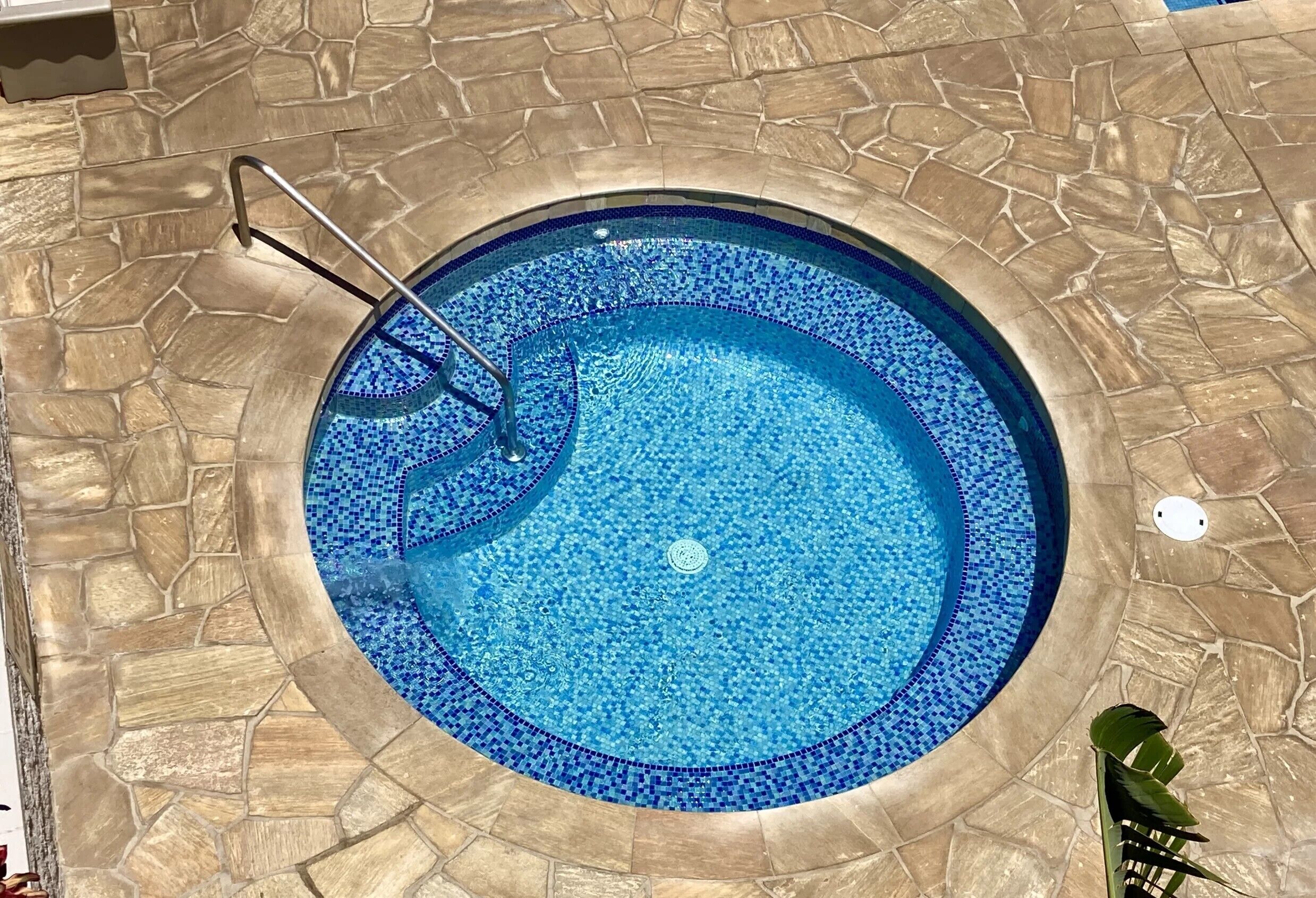 A circular pool with a mosaic tile border, surrounded by stone flooring.