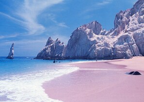A beach with a pink sand shore, clear blue water, and rocky cliffs in the background. - Cabo Condo 50 at the Marina! (Cabo San Lucas)