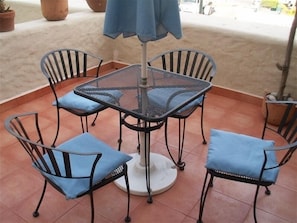 Un patio con una mesa redonda y cuatro sillas, cada una con un cojín azul.