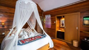 Une chambre à coucher avec un lit à baldaquin, des murs en bois, une petite salle de bain et un plancher en bois.