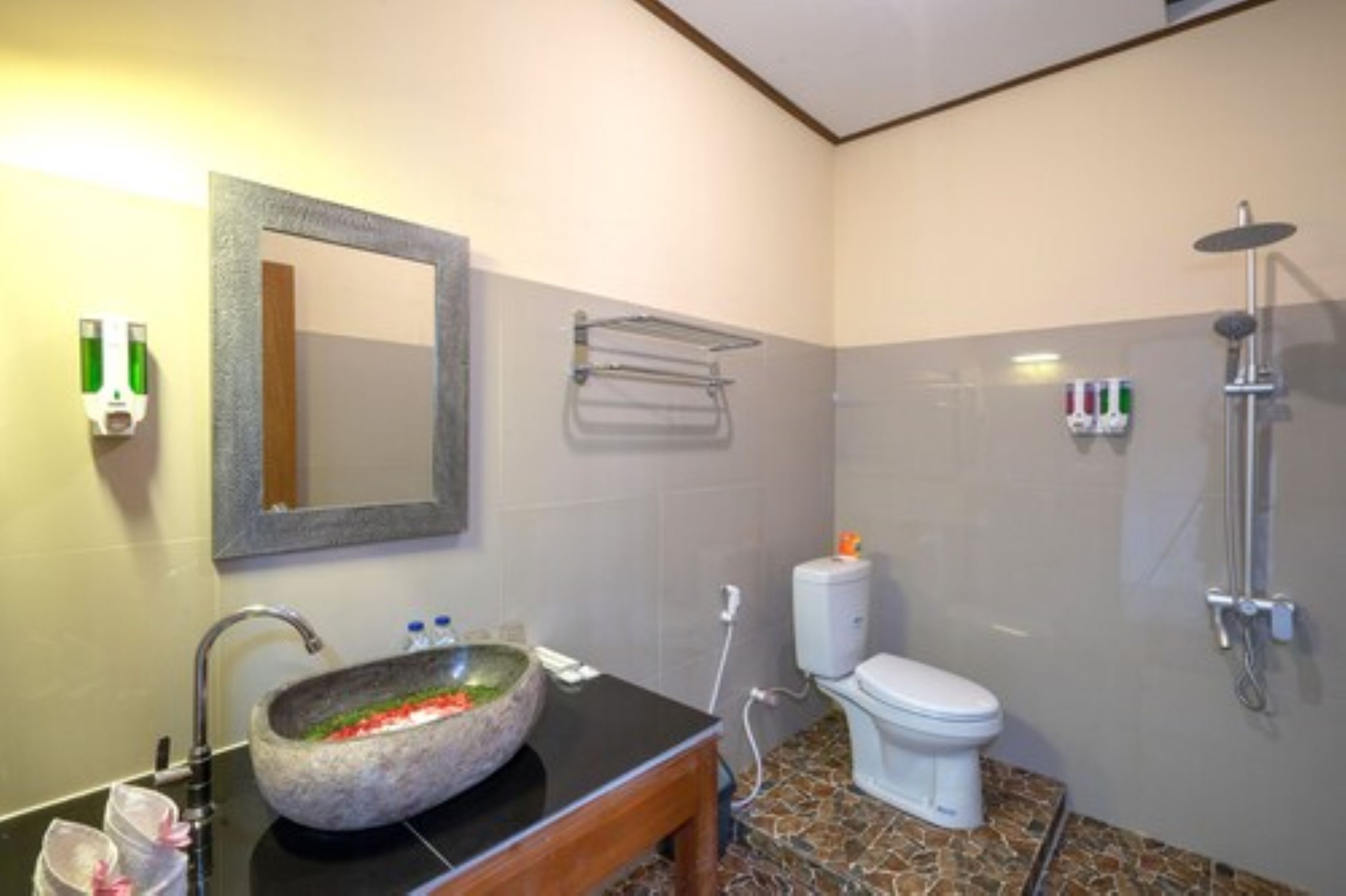 A bathroom with a stone sink, a mirror, a toilet, and a shower.