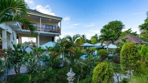 Une maison à deux étages dotée d’un balcon, entourée d’une végétation luxuriante et agrémentée d’une piscine.
