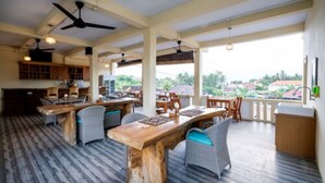 Un vaste espace intérieur comprenant plusieurs tables et chaises, un coin cuisine et un balcon offrant une vue sur le paysage environnant.