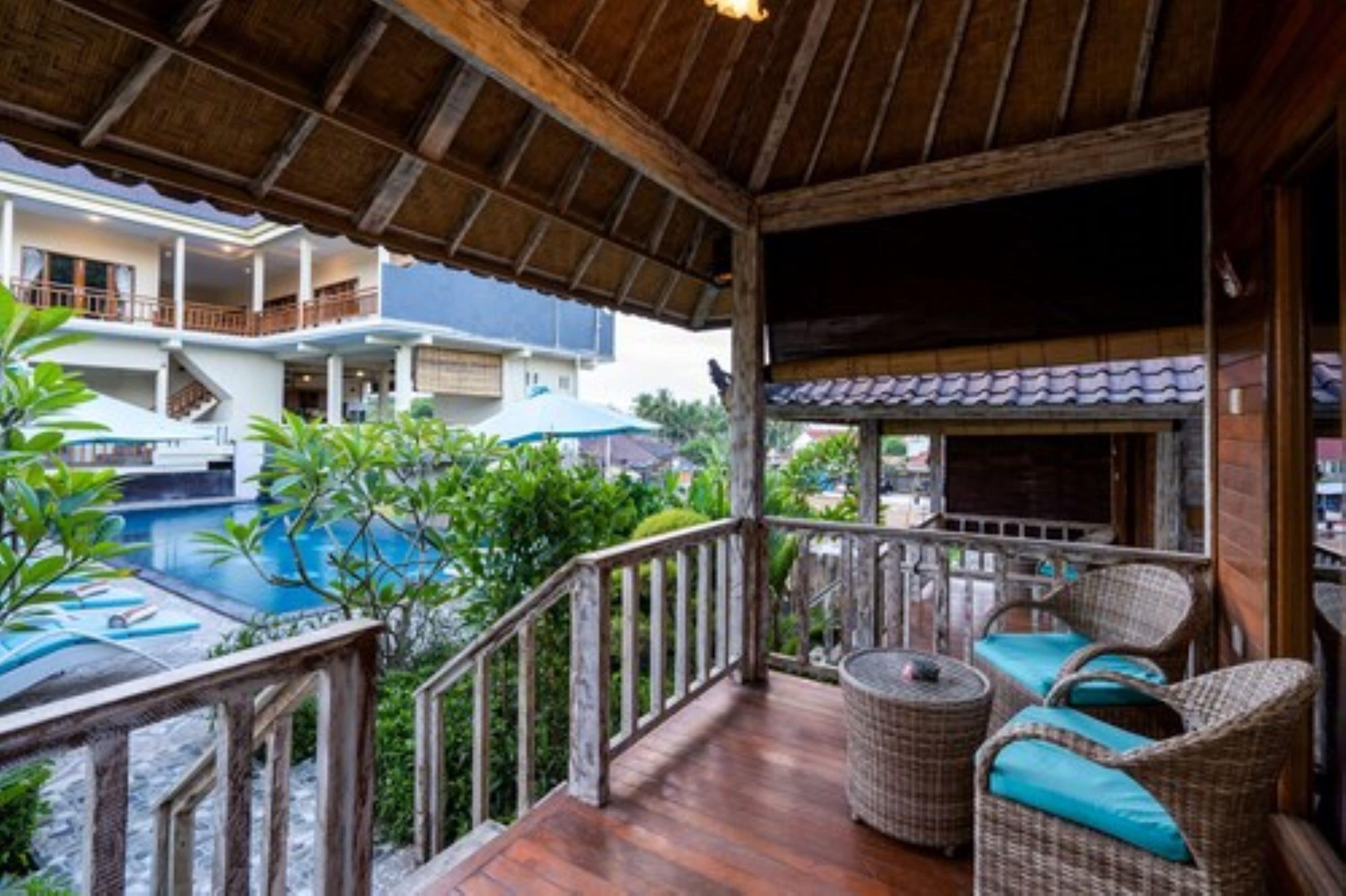 A wooden deck with wicker furniture, overlooking a swimming pool and lush greenery.